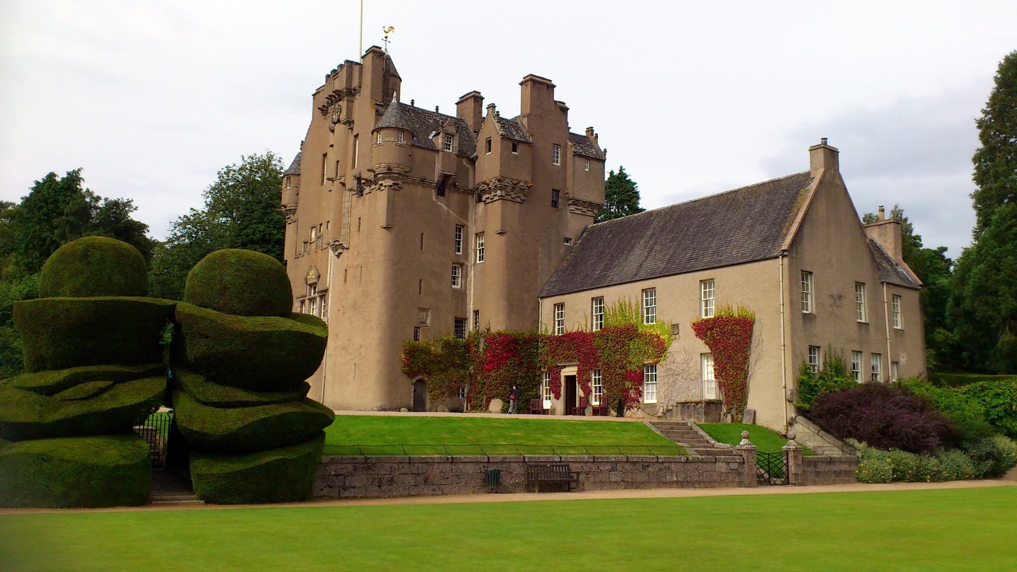 Crathes Castle tower house viewed across the formal garden with tall conifer trees.