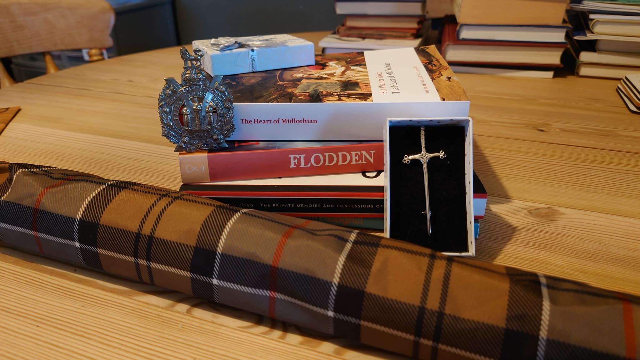 A King's Own Scottish Borderers badge, kilt pin, tartan umbrella and books on a wooden table.